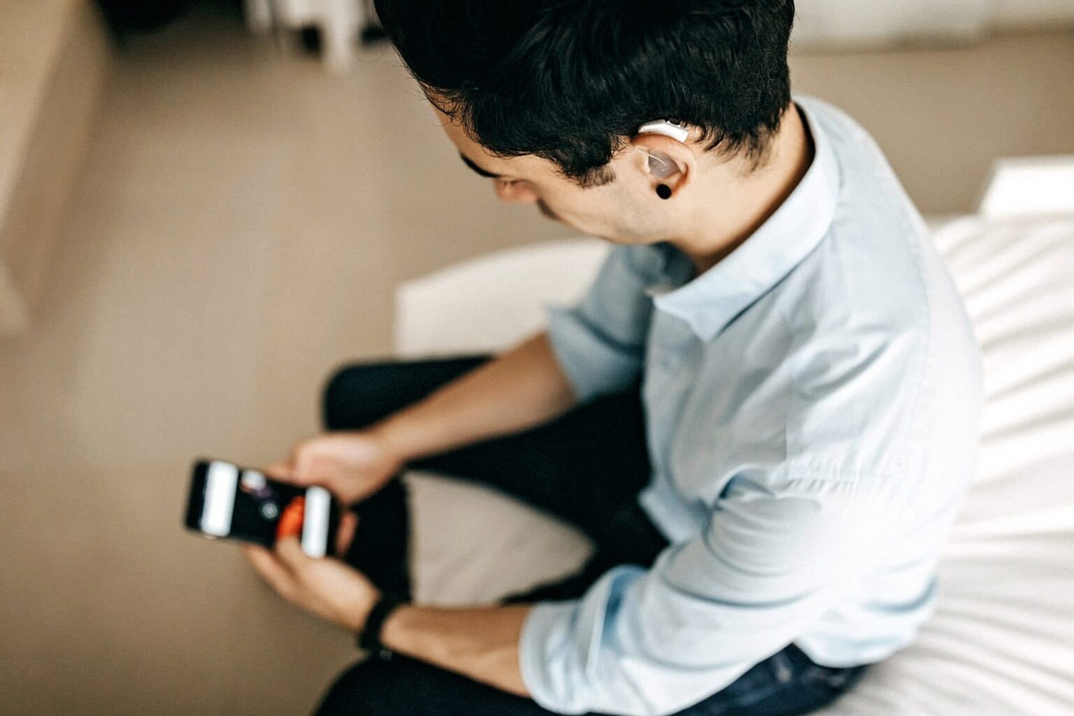 Younger man with a hearing aid using his smartphone.