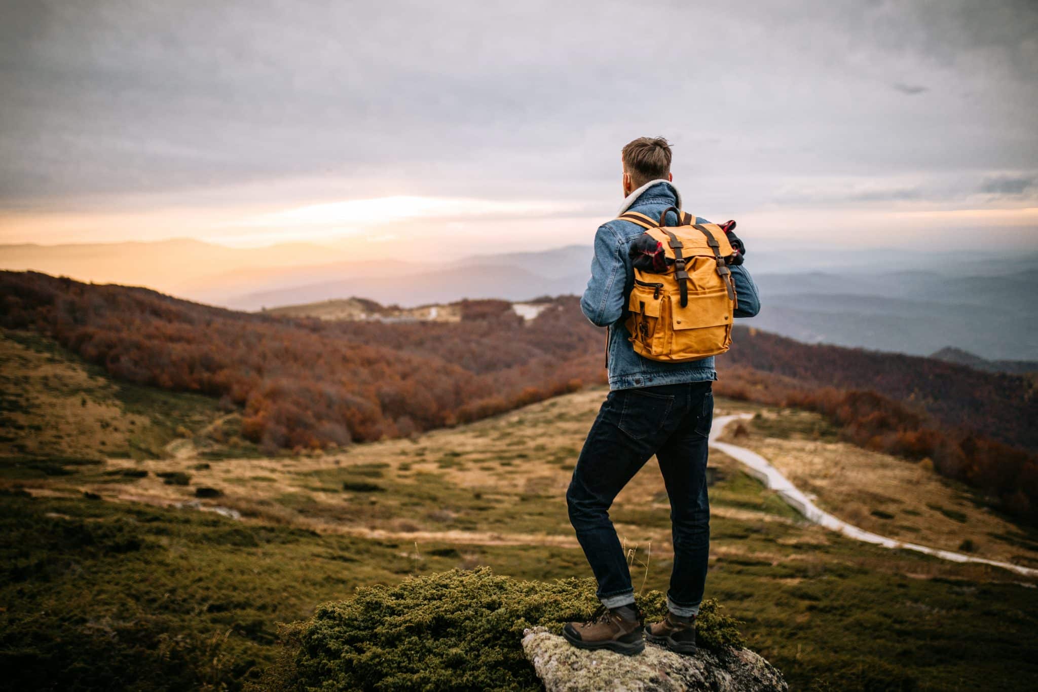 Young hiker standing on the mountain peak at the end of day, observing nature, enjoying the sunset.