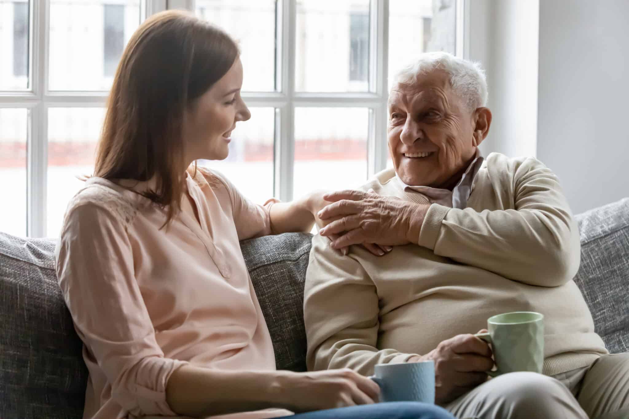 Adult woman talking to her senior father on the couch.