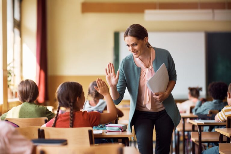 Happy teacher and schoolgirl giving high five during class at school. Student high-fiving her teacher in a classroom