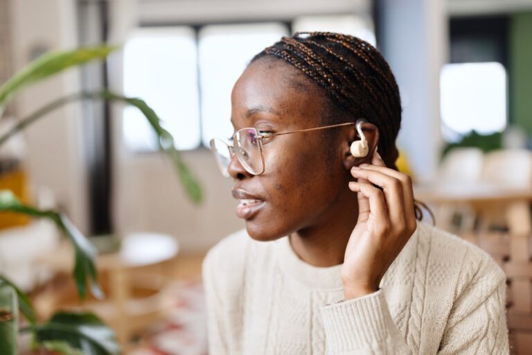 Woman adjusts hearing aid behind ear Woman adjusts hearing aid behind ear