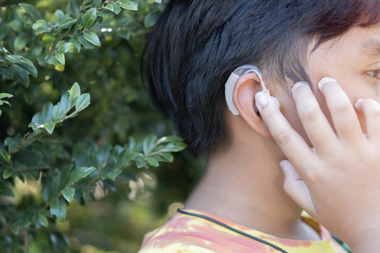 Boy readjusts hearing aid outside