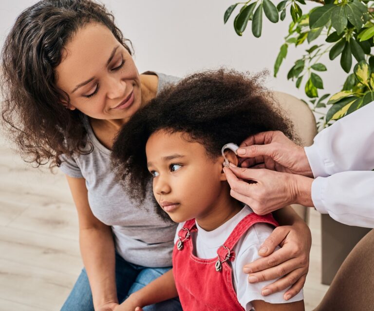 Parent helps child with hearing aid. Parent helps child with hearing aid.