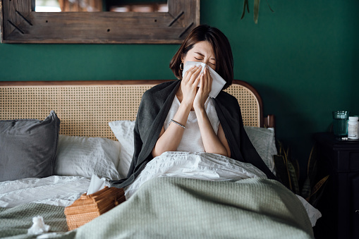 Woman sick with a viral infection, blowing her nose in bed.