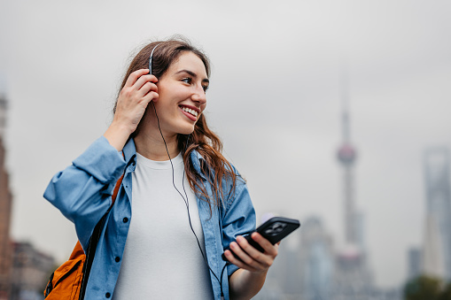 Smiling woman listening to music through her wired headphones connected to her smartphone