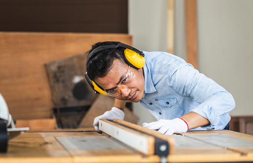 Man working in a woodshop wearing hearing and eye protection while using a saw.