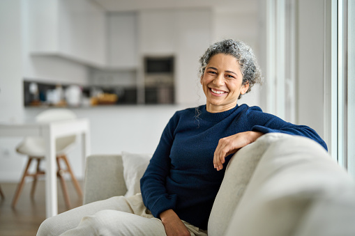 Confident, happy older woman who lives alone lounges in her living room.