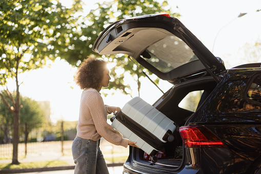 Person preparing for a vacation, loading a suitcase into the car. Another pre-vacation preparation could be checking your hearing health.