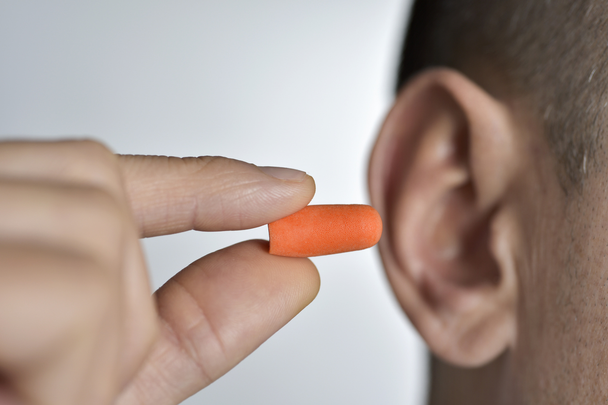Close-up of a hand holding up a foam earplug in front of an ear.